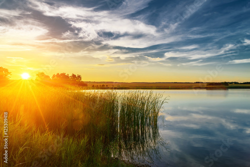 Summer sunset at the river with blue sky green trees and water w