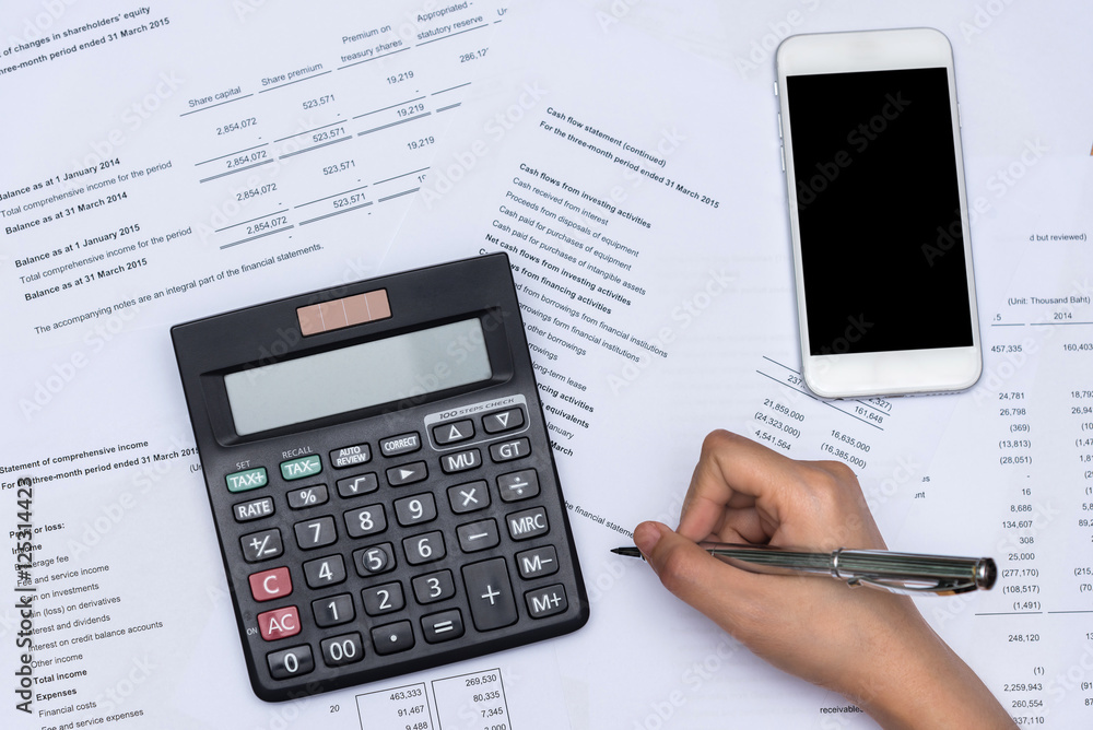 Top view of hand working with business financial data document with blank smart phone. Top view of hand working with business financial data document with blank smart phone.