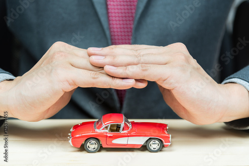 Businessman cover car model with his hands for protection. Car insurance concept