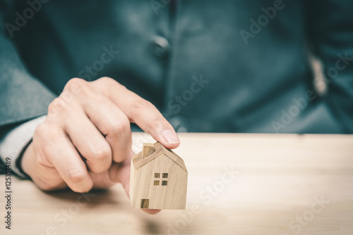 Businessman pick up and present wooden house model.
