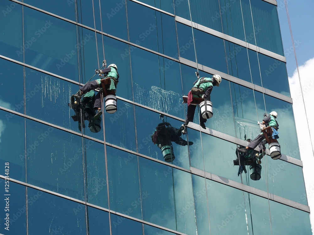 men cleaning glass building by rope access at height
