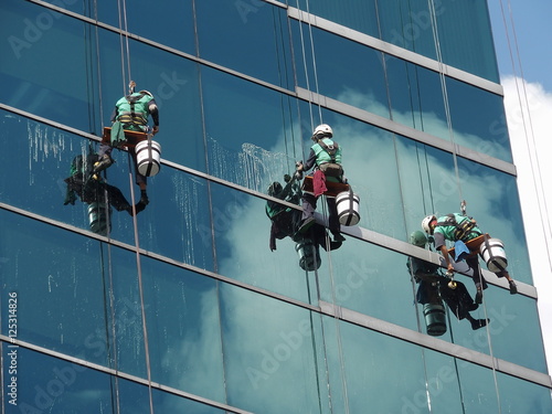 men cleaning glass building by rope access at height