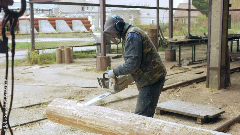 Man makes curly cutting wood Chainsaw. The log will be part of the future of the wooden house. Protective face mask on the face of the builder and a lot of sawdust. Man makes curly cutting wood Chainsaw. The log will be part of the future of the wooden house. Protective face mask on the face of the builder and a lot of sawdust.