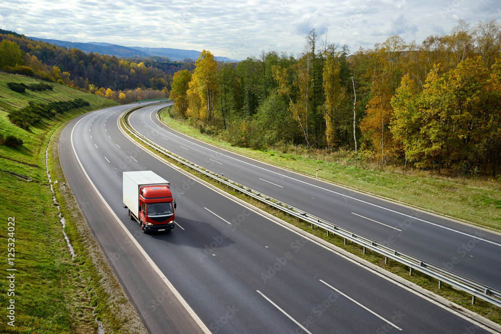 Asphalt road with a moving red small truck in the autumn landscape.
