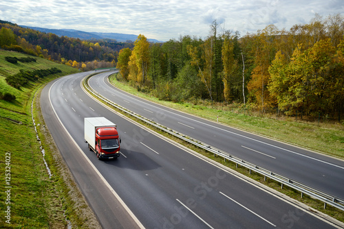 Asphalt road with a moving red small truck in the autumn landscape. © am