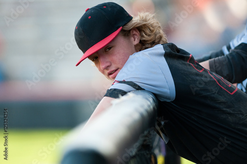Photography High school baseball player with long hair leaning on dugout fen