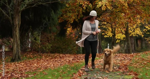 Woman walking golden retriever dog through a leaf covered park trail in Fall