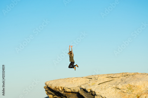 woman jumping for joy on a large rock on a sunny day