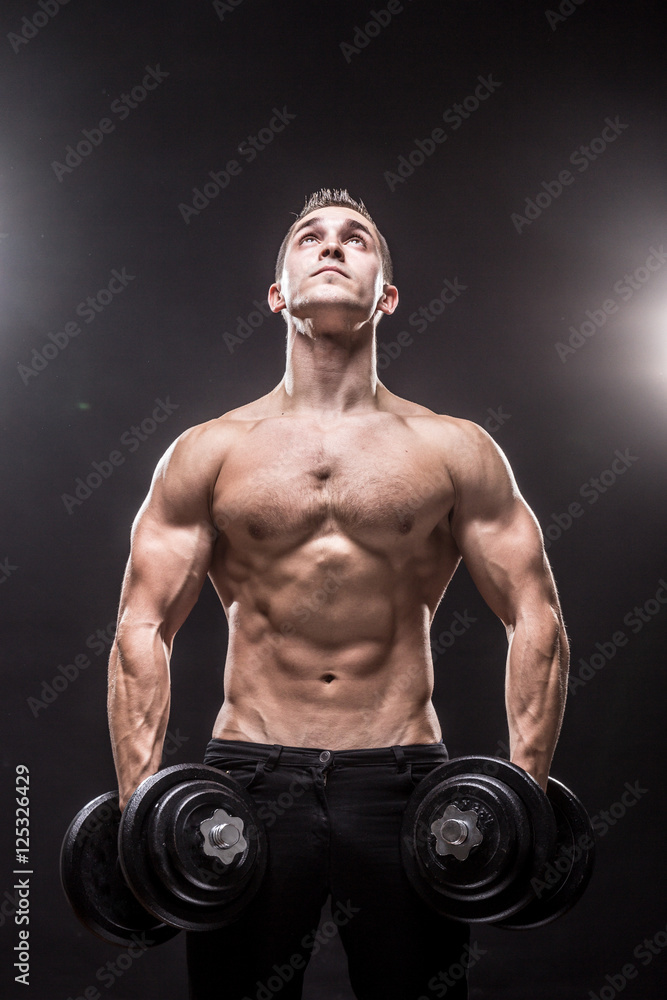 young man bodybuilder looking up dumbbells