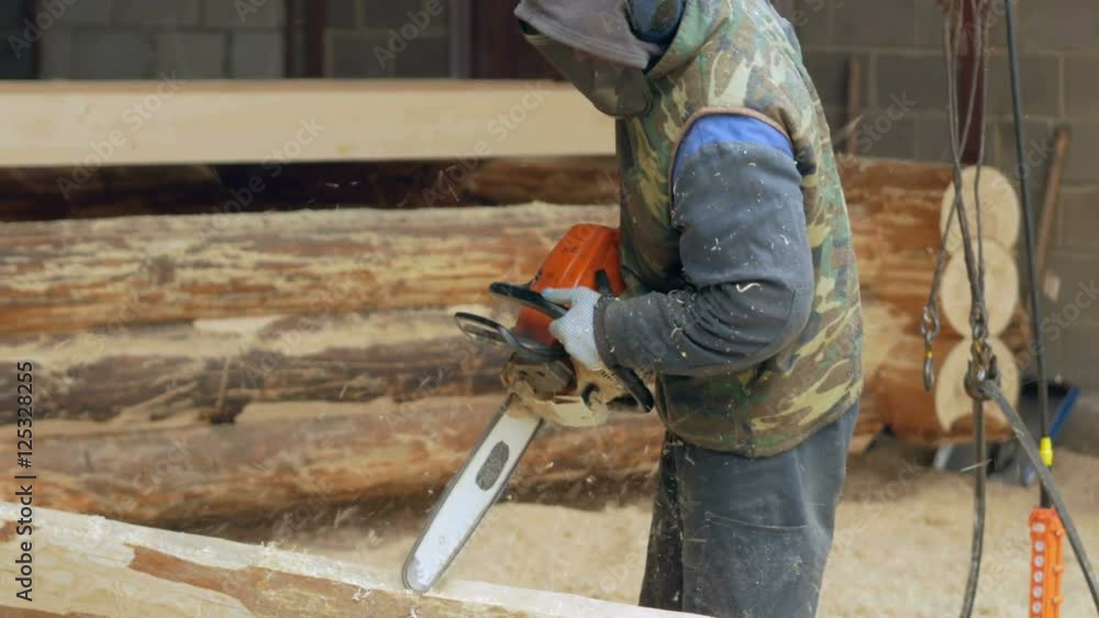 Man makes curly cutting wood Chainsaw. The log will be part of the future of the wooden house. Protective face mask on the face of the builder and a lot of sawdust. Man makes curly cutting wood Chainsaw. The log will be part of the future of the wooden house. Protective face mask on the face of the builder and a lot of sawdust.