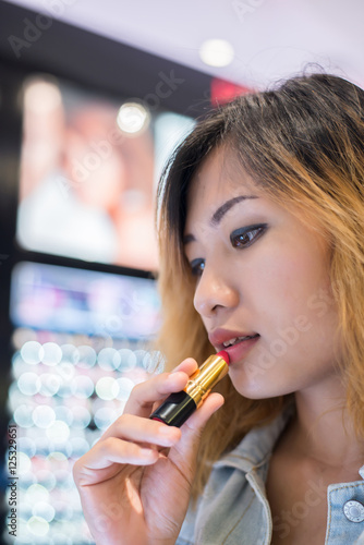 Beautiful young woman select color lipstick to buying at shoppin