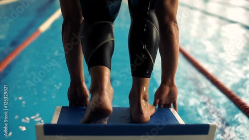 Professional concentrated male swimmer on starting block. Jump into water.