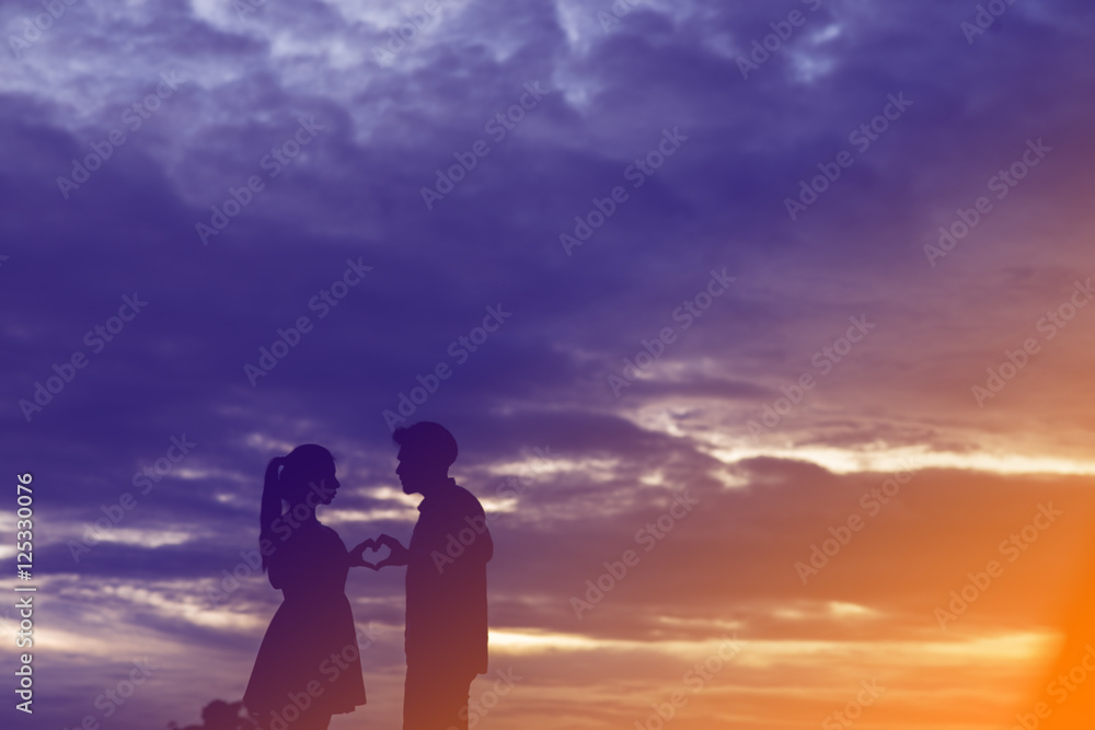 Man and woman holding hands in heart shape on the sunset backgro