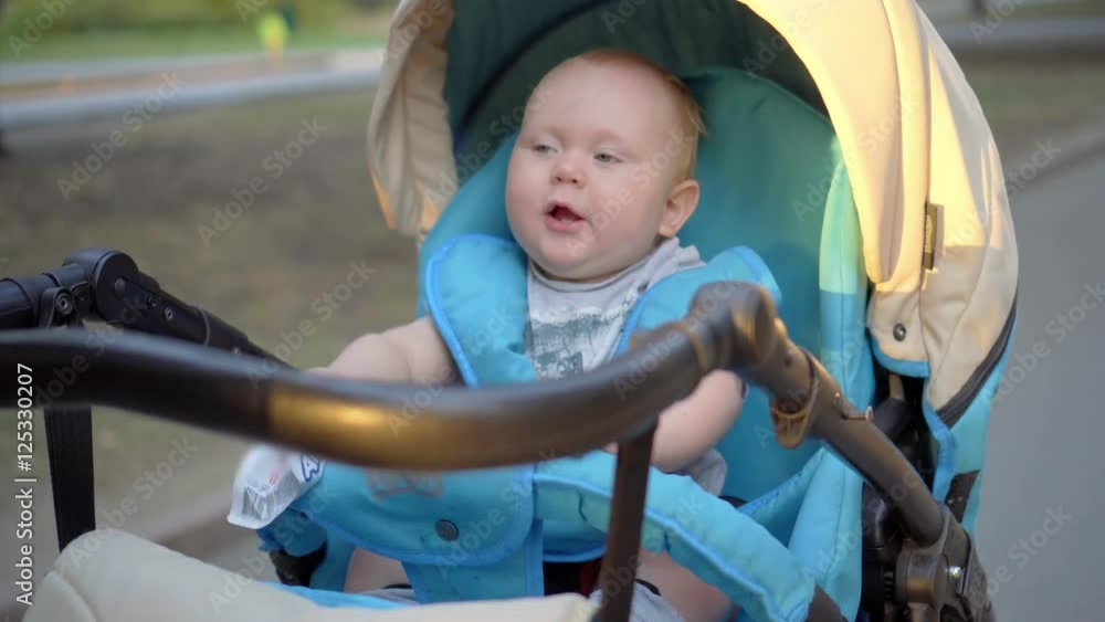 The kid rides in a carriage and waving hands of the packages with baby food in their hands. The kid rides in a carriage and waving hands of the packages with baby food in their hands.
