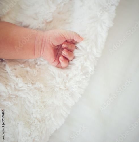 Newborn baby hand on white bed.