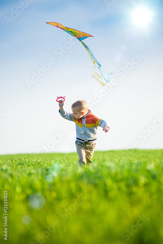 Young boy flies his kite in an open field. Little kid playing with kite on green meadow. Childhood concept.