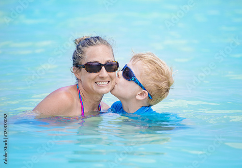 Mother and son playing together in an outdoor swimming pool. Boy kissing his smiling mom in the water. Fun time together © Brocreative