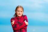 Outdoor portrait of cute little 9 year old girl wearing warm red knitted pullover, arms crossed, standing next to lake