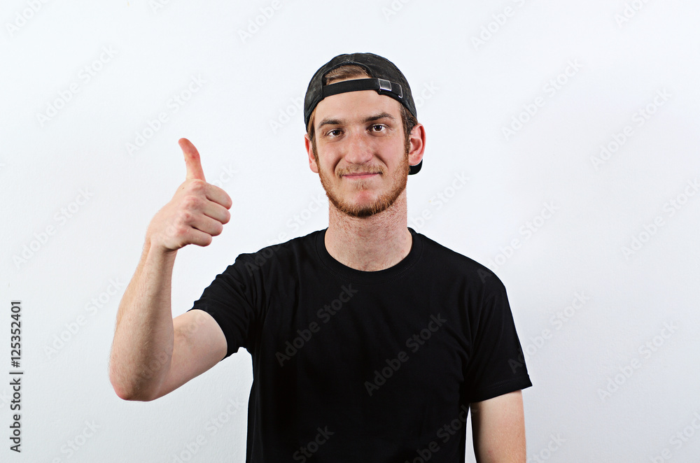 Smiling Young Adult Male in Dark T-Shirt and Baseball Hat Worn Backwards Shows His Thumbs Up Smiling Young Adult Male in Dark T-Shirt and Baseball Hat Worn Backwards Shows His Thumbs Up