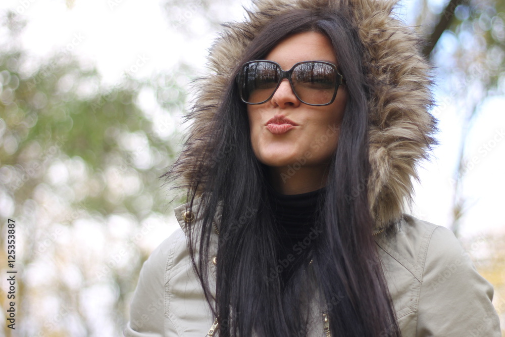 Beautiful woman with long dark hair giving kiss wearing hood in the autumn park Beautiful woman with long dark hair giving kiss wearing hood in the autumn park