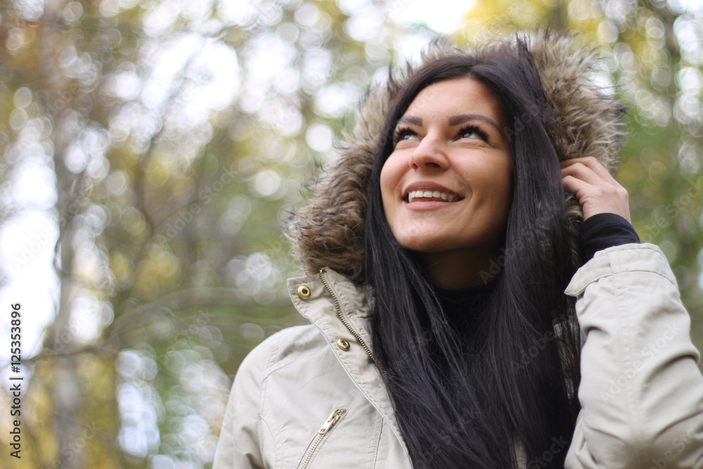 Beautiful woman with long dark hair wearing hood smiling in the autumn park Beautiful woman with long dark hair wearing hood smiling in the autumn park