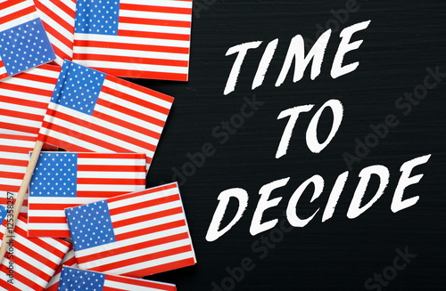 The words Time To Decide on a blackboard beside miniature flags of the United States of America as a reminder to vote in the Presidential elections
