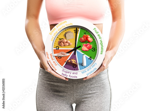 Beautiful, young woman holding a clock with food chart/eating schedule  photo