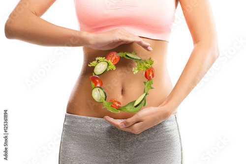 Fit, young woman holding a circle made out of vegetables over her abdomen 