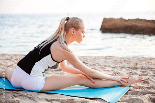 Young blonde woman doing stretching exercises on yoga mat