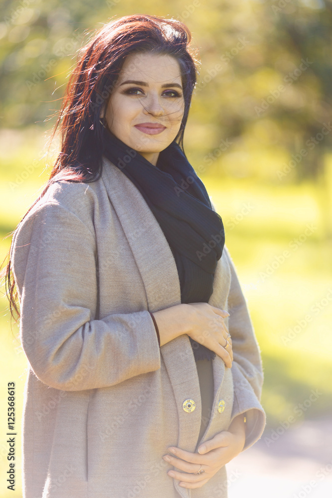 Beauty fashion pregnant brunette woman walking in the park outdoors
