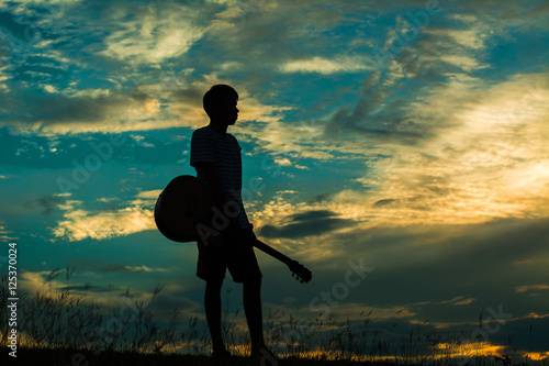 Man holding a guitar in the middle of a meadow silhouette