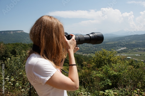 Young woman taking landscape photo with professional camera with telephoto lens