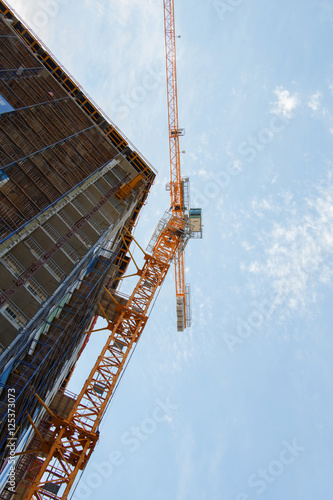 Yellow construction crane tower and incomplete building with blue sky at background. View from below