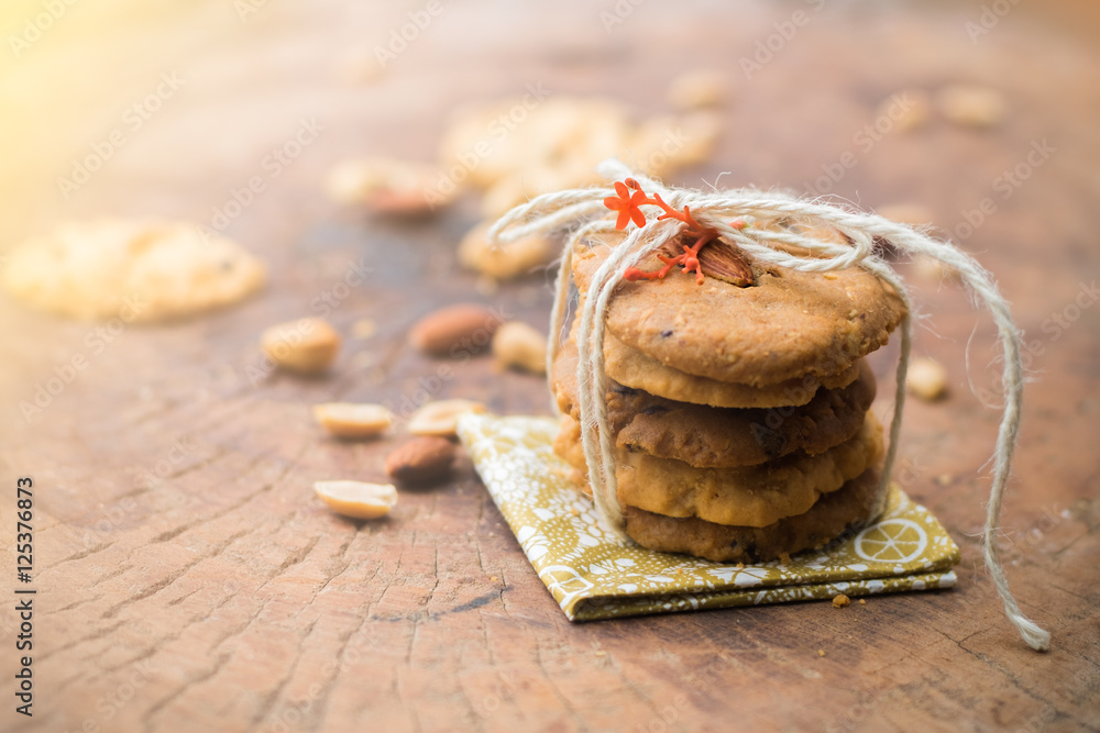 Stack of cookies with craft rope ribbon decorated by little orange flower on napkins with nuts and piece of cookie as blur background Stack of cookies with craft rope ribbon decorated by little orange flower on napkins with nuts and piece of cookie as blur background