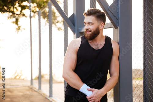 Smiling bearded athlete standing outdoors and looking away