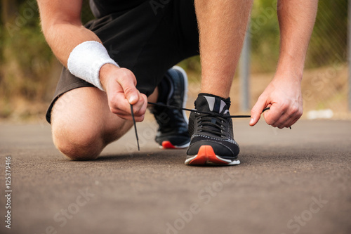 Handsome young sportsman tying shoelaces on his sneakers