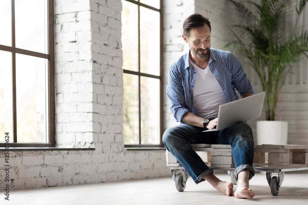 Positive delighted man holding a laptop on his knees Positive delighted man holding a laptop on his knees