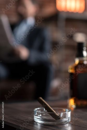 Selective focus of a cigar lying near the bottle