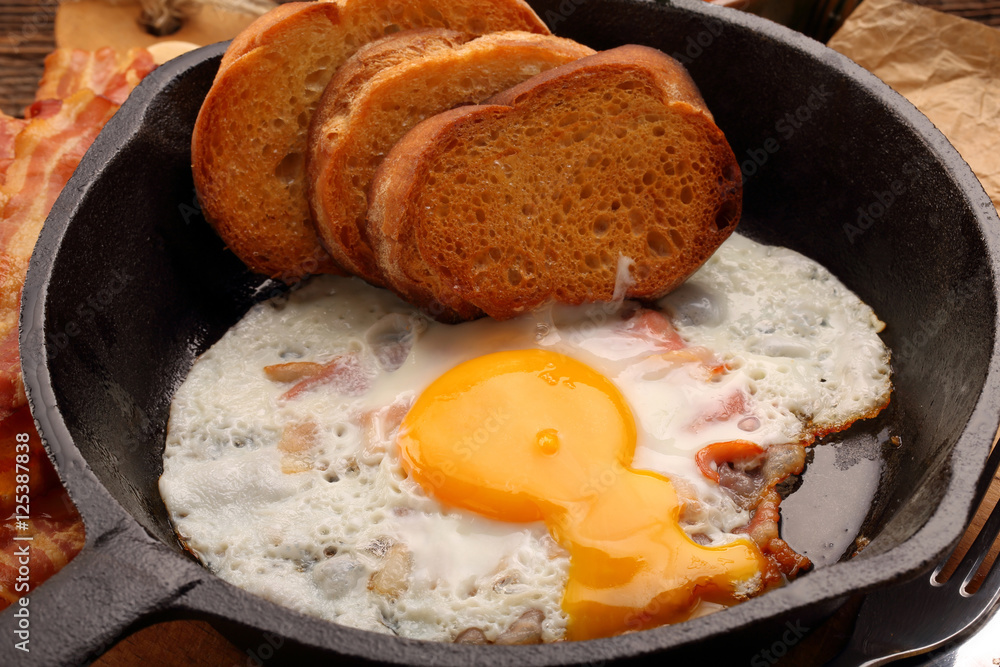 Fried egg with hot bacon pieces in a cast iron skillet