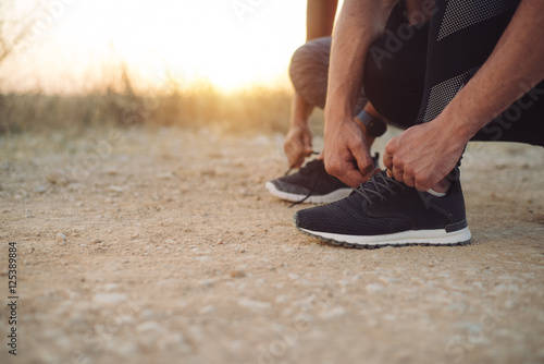 Outdoor running concept. Couple lacing sport shoes for preparing for training at sunset.