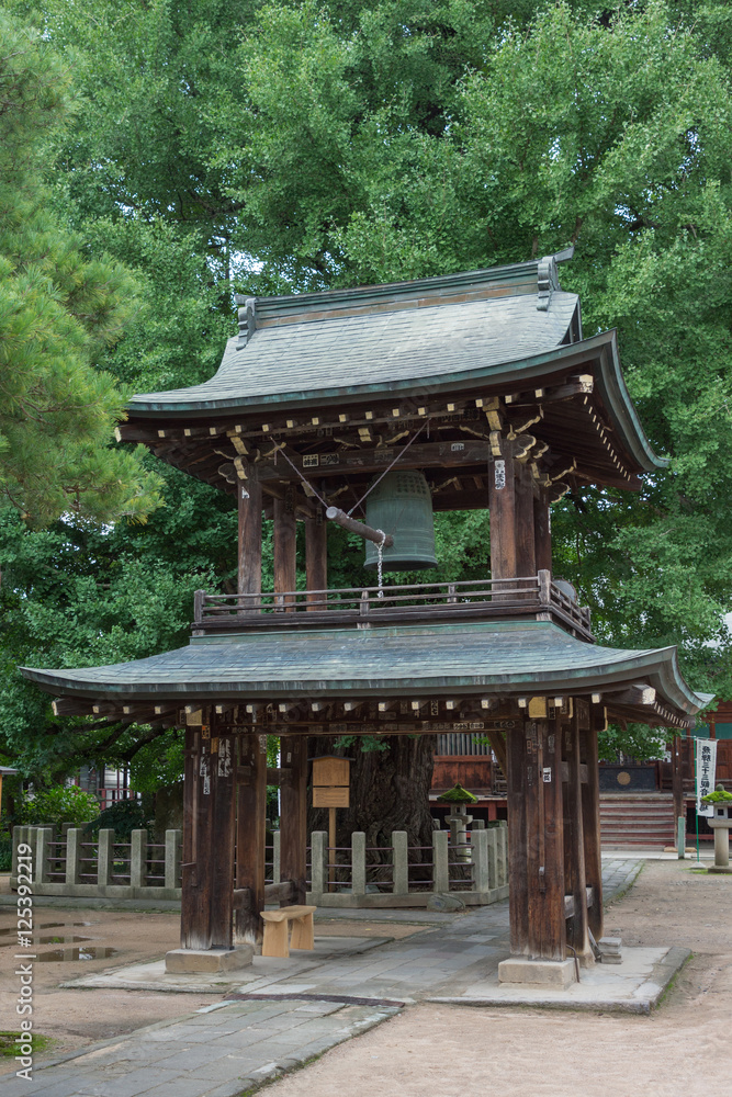 Takayama, Japan - September 24, 2016: Bell tower at Hikakokubun-ji Buddhist Temple has dark wood structure and bronze roofs under green trees. Takayama, Japan - September 24, 2016: Bell tower at Hikakokubun-ji Buddhist Temple has dark wood structure and bronze roofs under green trees.