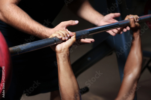 Personal coach helping man with barbell in gym