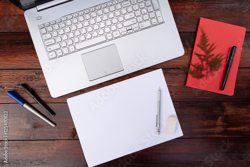 Place of work  blank sheet of paper with a pen. and laptop on a wooden desk -  Mock up