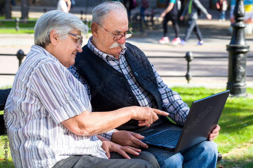 happy seniors couple with notebook sitting on a bench in a park in spring happy seniors couple with notebook sitting on a bench in a park in spring
