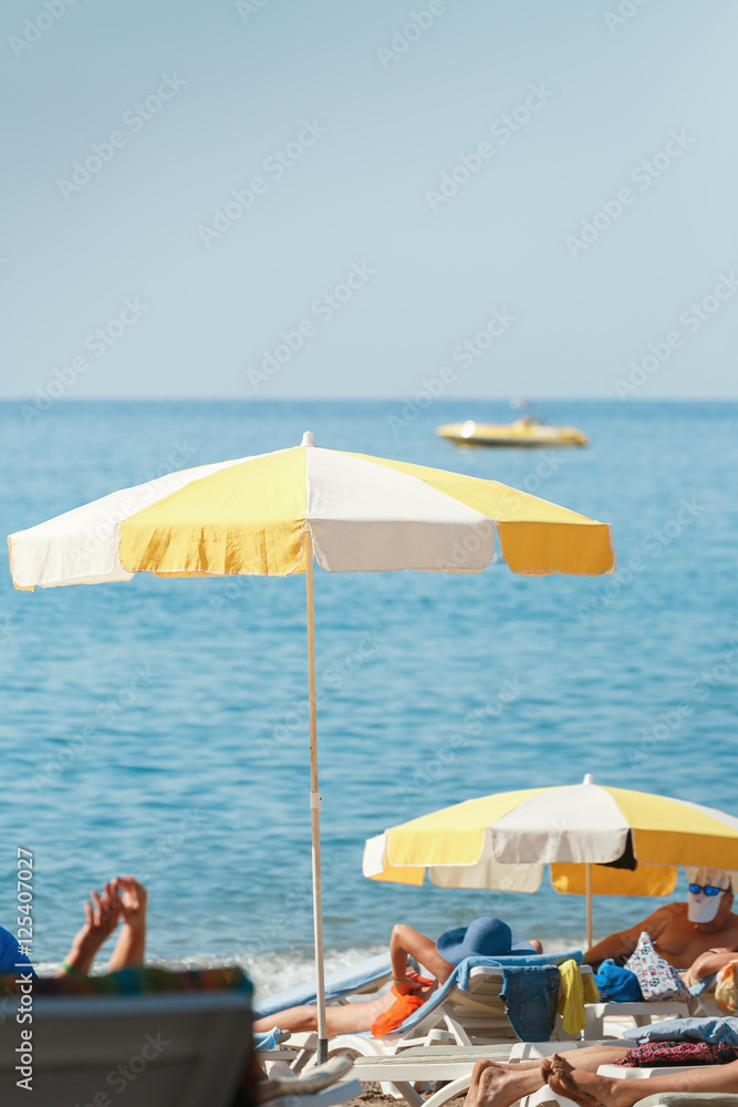Umbrella sea beach, people lying on sun loungers