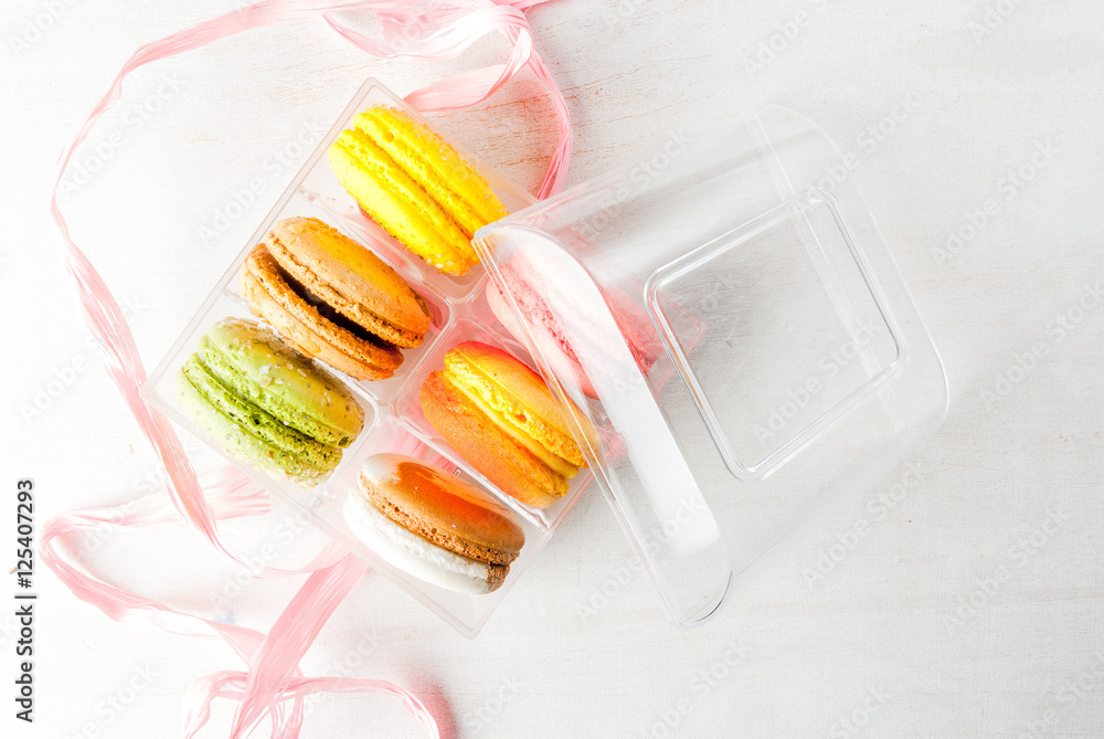 Open a transparent gift box with cakes macarons on a white wooden table. Top view, copy space Open a transparent gift box with cakes macarons on a white wooden table. Top view, copy space