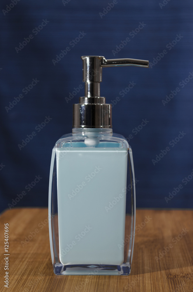 Light blue liquid soap dispenser with a chrome top on a wooden shelf with a dark blue background Light blue liquid soap dispenser with a chrome top on a wooden shelf with a dark blue background
