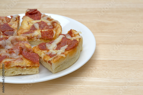 Personal size pepperoni pizza slices on a white plate atop a wood table.