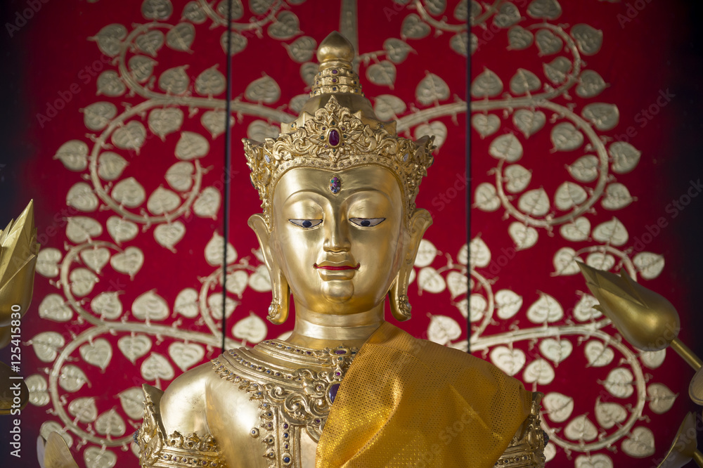 Golden buddha with sash close up against a bright decorative floral patterned background in a Buddhist temple in Bangkok Thailand