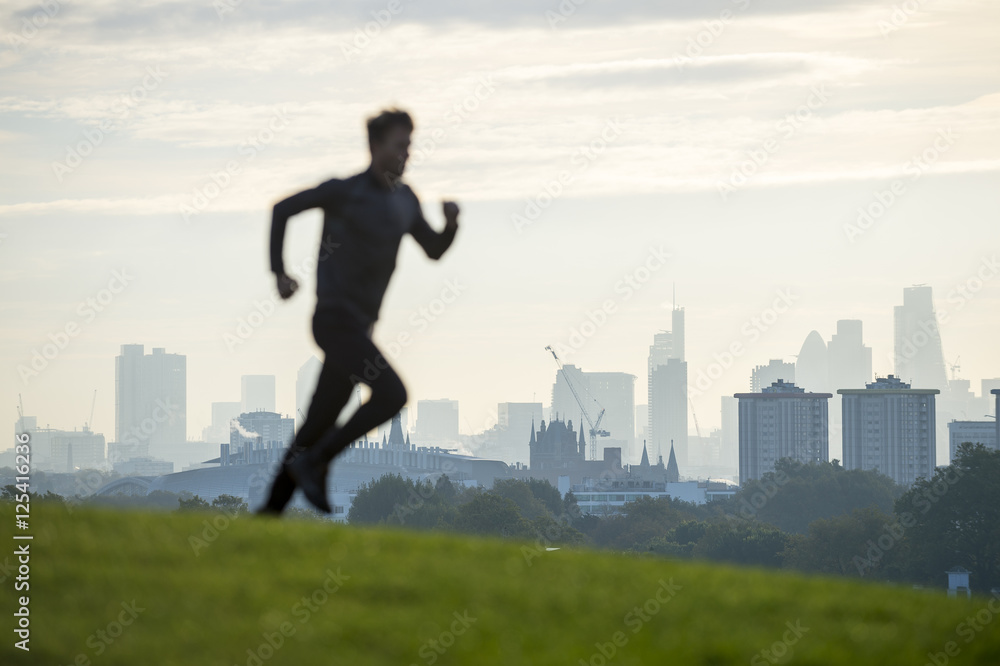 Abstract silhouette of jogger running on the green grass of Primrose Hill in front of the misty London city skyline